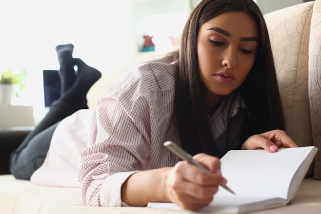 Portret Uśmiechniętej Pięknej Kobiety Piszącej Notatki W Notatniku Leżącym Na Kanapie W Domu