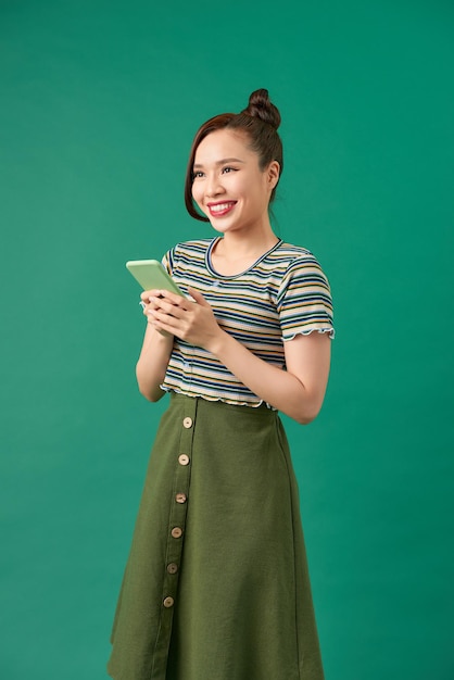 Portret uśmiechniętej przypadkowej kobiety trzymającej smartfon na zielonym tle