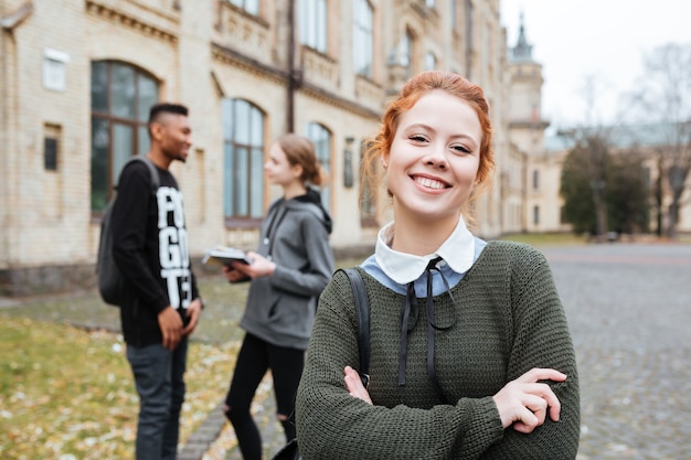 Portret Uśmiechniętej Rudej Studentki Stojącej Na Kampusie Uniwersyteckim Z Założonymi Rękami