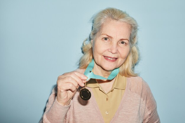 Portret uśmiechniętej starszej kobiety noszącej medal i patrzącej na kamerę stojąc na niebieskim tle, kopia przestrzeń