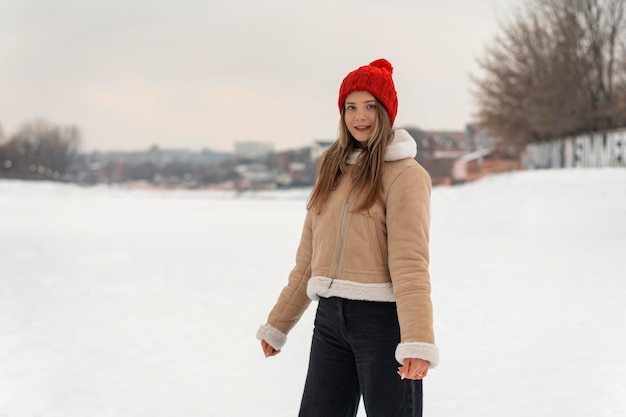 Portret uśmiechniętej uczennicy lub studenta w czerwonym kapeluszu z dzianiny i kożuchu Chodzenie w zimowym parku pokrytym śniegiem