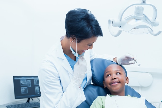 Portret uśmiechnięty żeński dentysta egzamininuje chłopiec zęby