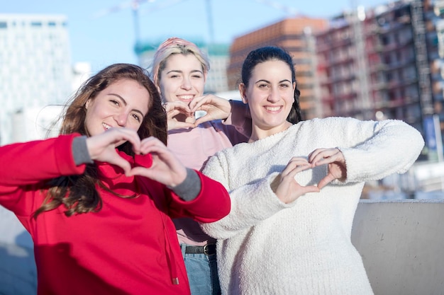 Zdjęcie portret uśmiechniętych młodych kobiet tworzących kształt serca rękami, stojąc w mieście