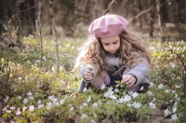Portret w stylu vintage ubrana mała dziewczynka gra w lesie z kwiatami