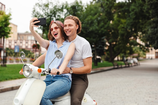 Portret wesoła młoda para razem na motocyklu na ulicy miasta, robienie selfie