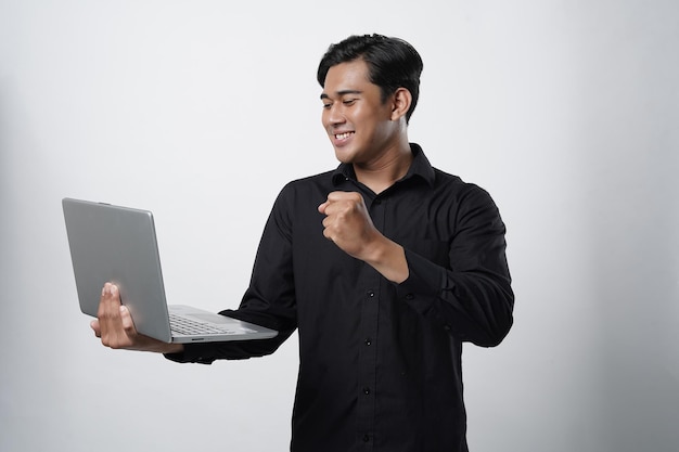 Portret wesołego azjatyckiego tysiącletniego faceta używającego laptopa do pracy online z gestem sukcesu