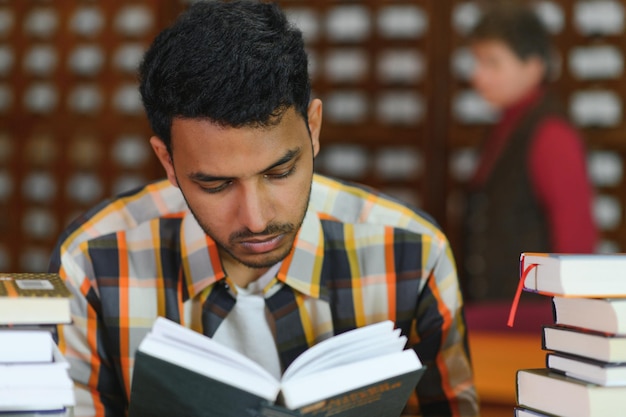 Portret wesołego męskiego międzynarodowego indyjskiego studenta z akcesoriami do nauki plecaka stojącego w pobliżu półek na książki w bibliotece uniwersyteckiej lub księgarni podczas przerwy między lekcjami Koncepcja edukacji