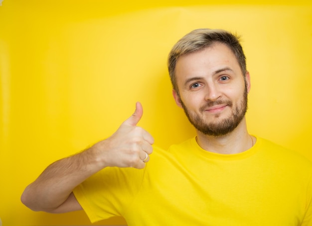 Portret wesołego mężczyzny w żółtych ubraniach i pokazujący kciuki do góry na żółtym tle