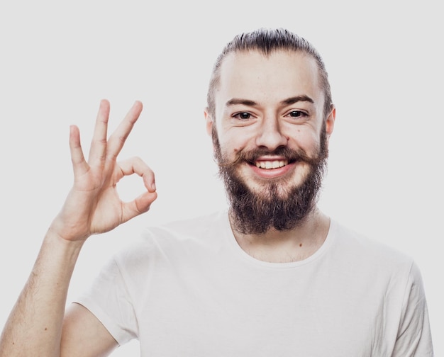 Portret wesołego młodego brodatego mężczyzny pokazującego dobry gest na białym tle