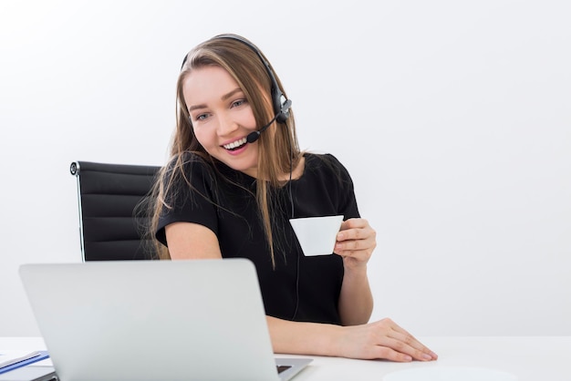 Portret wesołego pracownika call center trzymającego filiżankę kawy i patrzącego na ekran laptopa z szerokim uśmiechem.