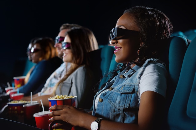 Portret wesołej afrykańskiej kobiety uśmiechającej się radośnie podczas oglądania filmu w miejscowym kinie