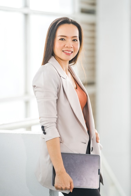 Portret wesołej azjatyckiej kobiety biznesu trzyma na wynos kawę i cyfrowy tablet w firmie