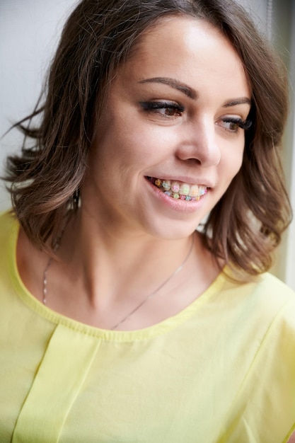 Portret wesołej kobiety z ortodontycznymi nawiasami Wesoła kobieta z brązowymi włosami pokazująca nawiasy z wielokolorowymi gumkami na zębach Koncepcja stomatologii i leczenia ortodontycznego