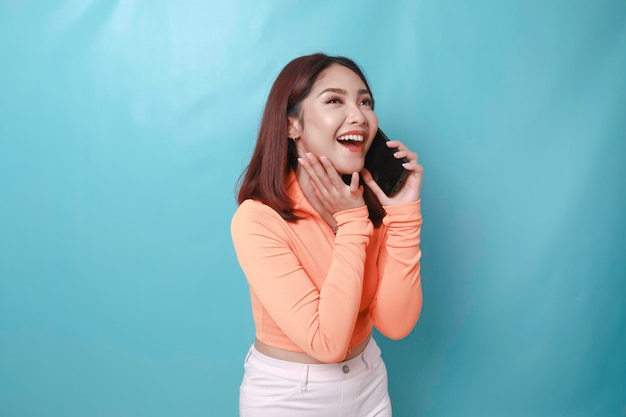 Portret wesołej młodej azjatyckiej kobiety, która rozmawia przez telefon na niebieskim tle