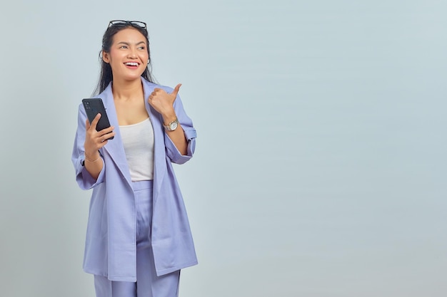 Portret wesołej młodej azjatyckiej kobiety trzymającej telefon komórkowy i pokazującej miejsce na kopię na białym tle