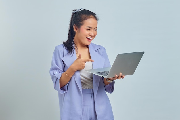 Portret wesołej młodej azjatyckiej kobiety wskazującej palcami na laptopie na białym tle