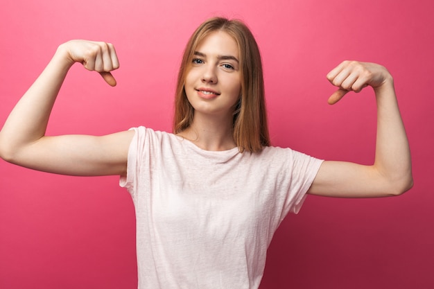 Portret wesoły młoda dziewczyna gięcia bicepsów na różowej ścianie, ładny i atrakcyjny
