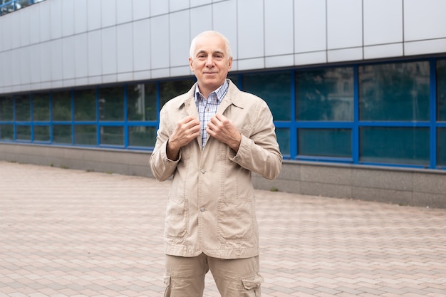 Portret wesoły starszy biznesmen w przypadkowy strój stojący na ulicy miasta