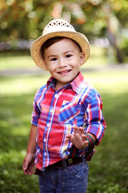 Portret wesoły szczęśliwe dziecko w słomkowym kapeluszu, grając w parku latem.