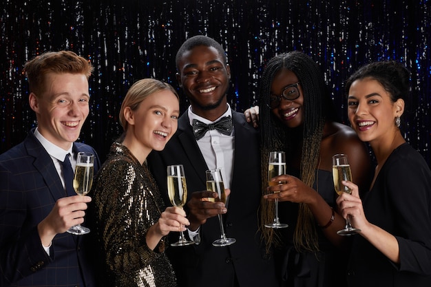 Zdjęcie portret wieloetnicznej grupy przyjaciół trzymających kieliszki do szampana i uśmiechając się do kamery, ciesząc się elegancką imprezą