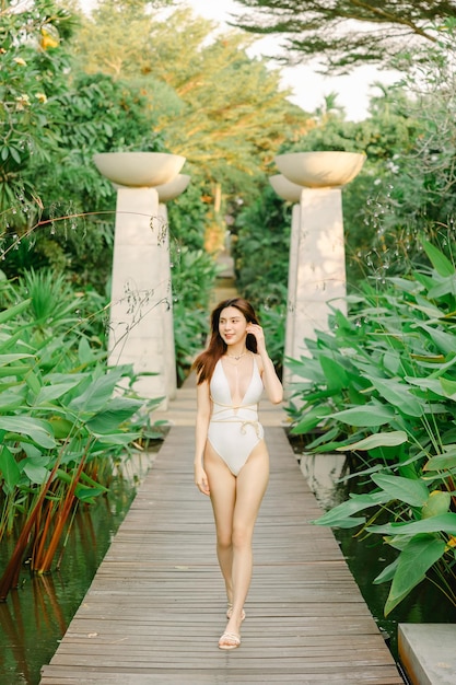 Portret wspaniałej azjatyckiej modelki piękna opalenizna do pielęgnacji skóry spacerująca po tropikalnym ogrodzie w białym jednoczęściowym stroju kąpielowym relaksująca się na plaży w letnim kurorcie Spa laser wellness