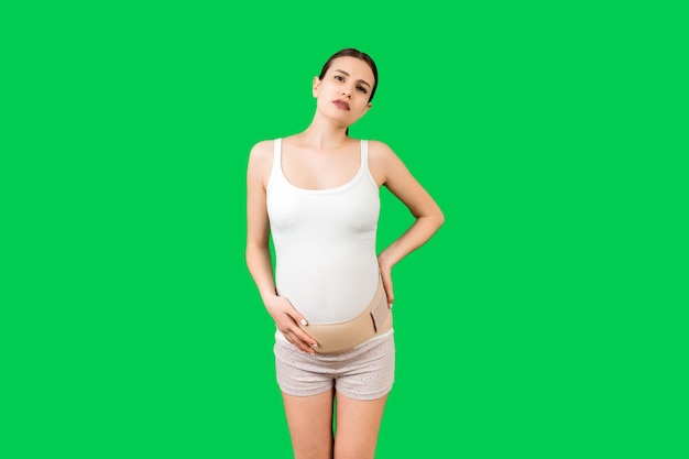 Portret wspierający bandaż przeciw bólom pleców na kobietę w ciąży na zielonym tle z miejsca na kopię. Matka cierpi na ból pleców. Koncepcja ortopedycznego pasa podtrzymującego brzuch.