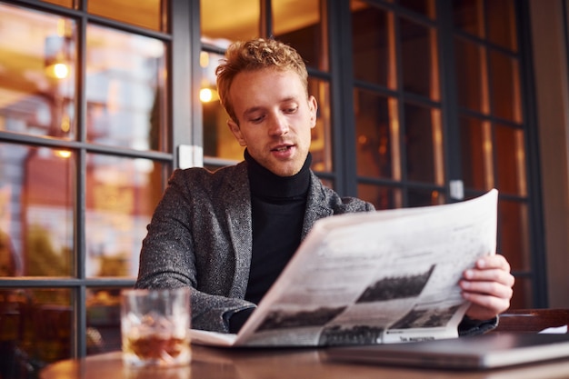 Portret współczesnego młodego faceta w formalne ubrania, który siedzi w kawiarni i czyta gazetę.