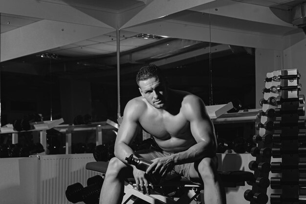 Zdjęcie portret wysportowanego mężczyzny z butelką białka bez koszuli mężczyzna z mięśniami tułowia na siłowni