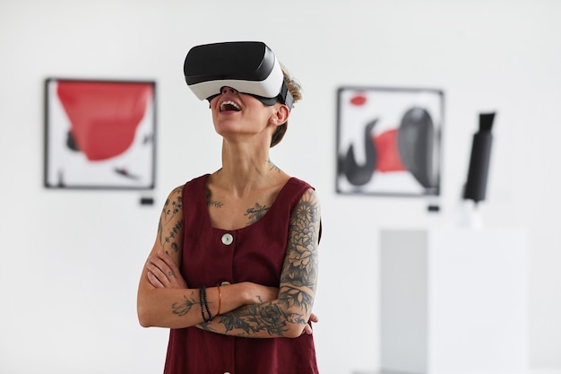 Portret wytatuowanej młodej kobiety noszącej sprzęt VR, ciesząc się wciągającymi wrażeniami na wystawie galerii sztuki współczesnej,
