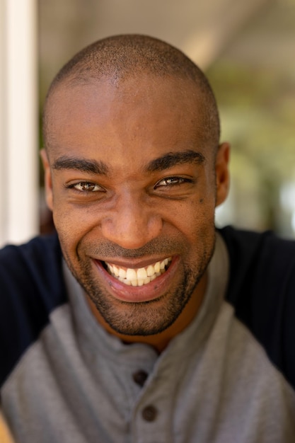 Portret z bliska Afroamerykanina z krótkimi włosami siedzącego na zewnątrz i uśmiechającego się do kamery.