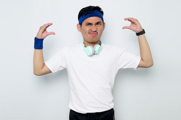 Portret zabawny młody azjatycki sportowiec w niebieski pałąk i odzież sportowa biała koszulka ze słuchawkami ręka gest konwersacji na białym tle Koncepcja sportu treningu