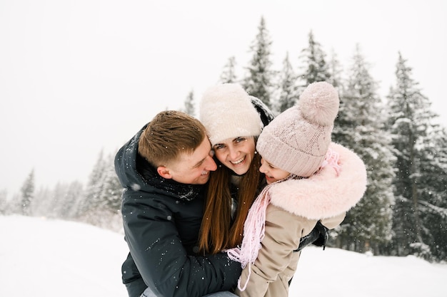 Portret zabawny szczęśliwa rodzina w zimowym lesie. Matka, ojciec i córka bawią się śniegiem. Cieszyć się spędzaniem czasu razem. Koncepcja rodziny
