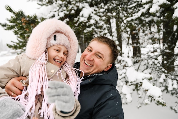 Portret zabawny szczęśliwa rodzina w zimowym lesie. Ojciec i córka przytulają się i bawią się śniegiem. Pojęcie rodziny. Cieszyć się spędzaniem czasu razem