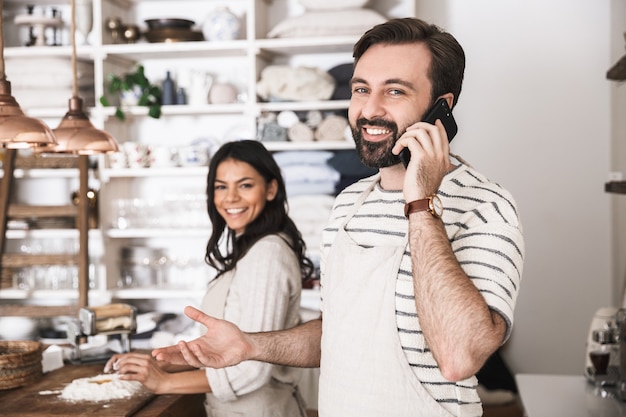 Portret zadowolonej pary mężczyzny i kobiety w wieku 30 lat w fartuchach za pomocą smartfona podczas wspólnego gotowania w kuchni w domu
