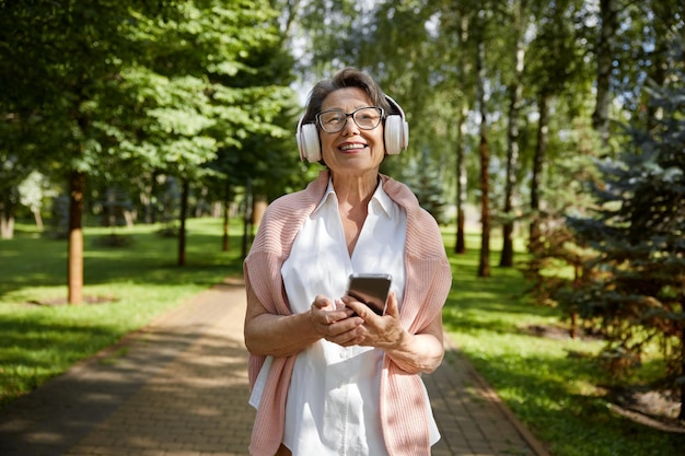 Portret zadowolonej starej kobiety korzystającej z telefonu komórkowego cieszącej się letnim dniem podczas spaceru w parku publicznym