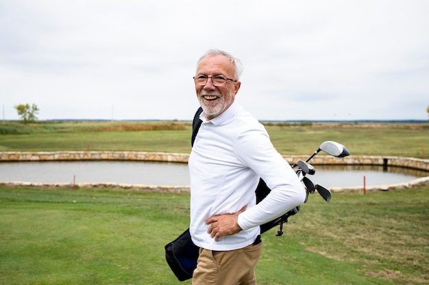 Portret zamożnego starszego golfisty z kijami golfowymi, ciesząc się wolnym czasem na świeżym powietrzu.