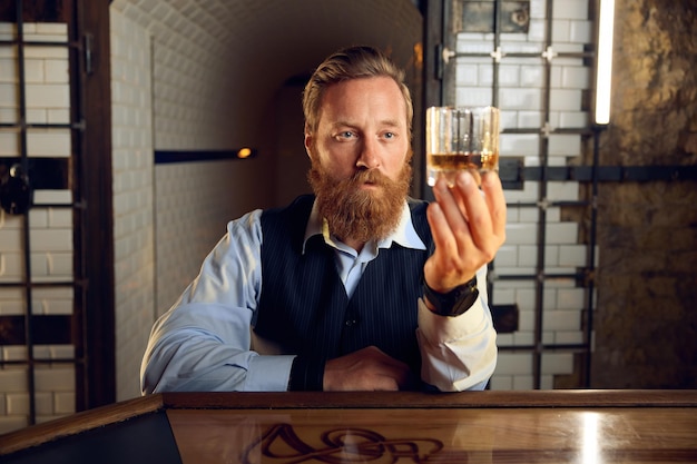 Zdjęcie portret zamyślonego eleganckiego mężczyzny patrzącego przez szklankę whisky. koncepcja nadużywania alkoholu