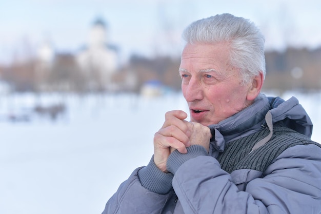 Portret zamyślonego starszego mężczyzny w pokrytym śniegiem zimowym parku