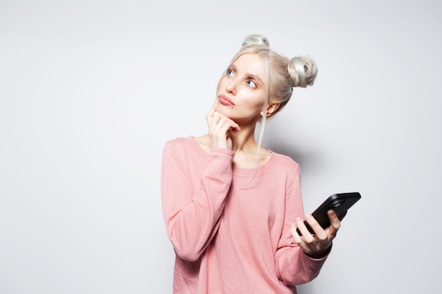 Portret zamyślonej ślicznej blondynki ze smartfonem w ręku na białym