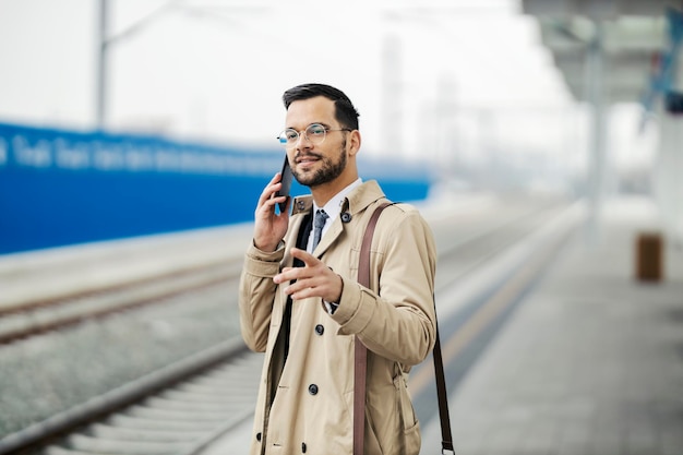 Portret zapracowanego młodego mężczyzny w eleganckim swobodnym stylu rozmawiającego przez telefon podczas oczekiwania na metro