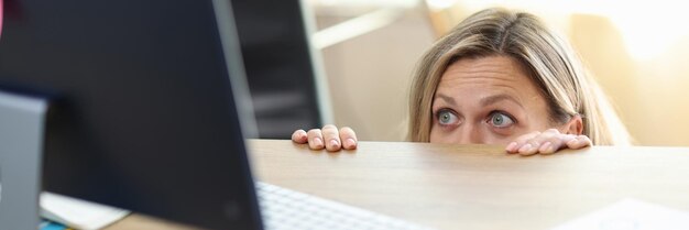 Portret zaskoczonej i podekscytowanej kobiety wyglądającej z biurka i patrzącej na biuro na ekranie komputera