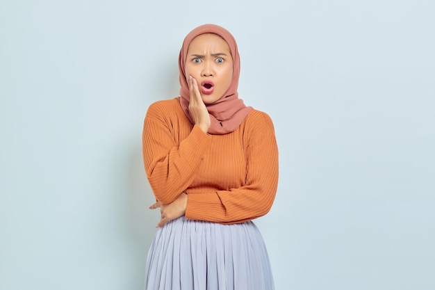 Portret zaskoczonej młodej azjatyckiej muzułmanki z otwartymi ustami i patrzącej na kamerę na białym tle