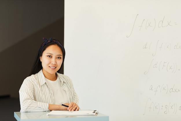Portret zawartości atrakcyjna dziewczyna azjatyckich studentów stojących na stoisku wykładowym z papierami przed tablicy w klasie