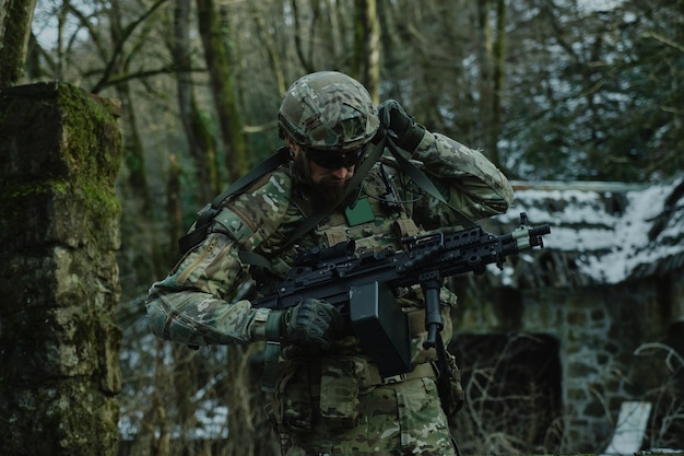 Portret zawodnika airsoft w profesjonalnym sprzęcie z karabinem maszynowym w lesie. Żołnierz z bronią na wojnie