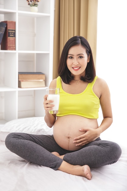 Portret zdrowej kobiety w ciąży trzymając szklankę mleka, siedząc na łóżku w domu