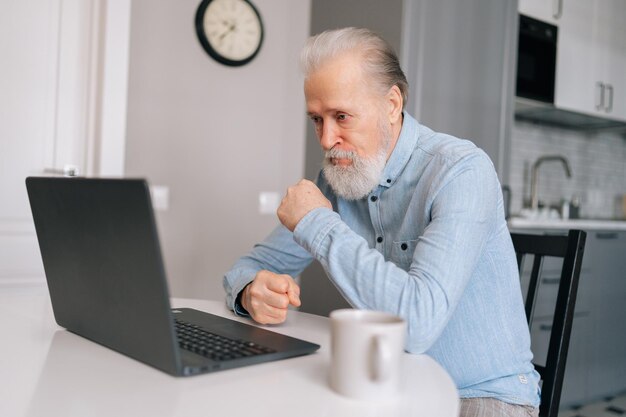 Portret zirytowanego starszego starszego biznesmena słuchającego towarzysza biznesowego podczas rozmowy wideo na laptopie i ledwo może powstrzymać się od przeklinania