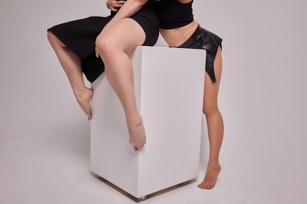 Portret zmysłowej nastolatki siedzącej na jednej nodze, opierając się na białym kwadratowym panelu