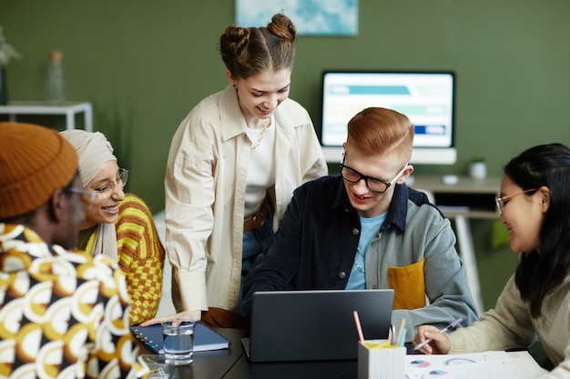 Portret zróżnicowanego zespołu kreatywnego korzystającego z laptopa podczas spotkania biznesowego, cieszącego się wspólną pracą nad projektem