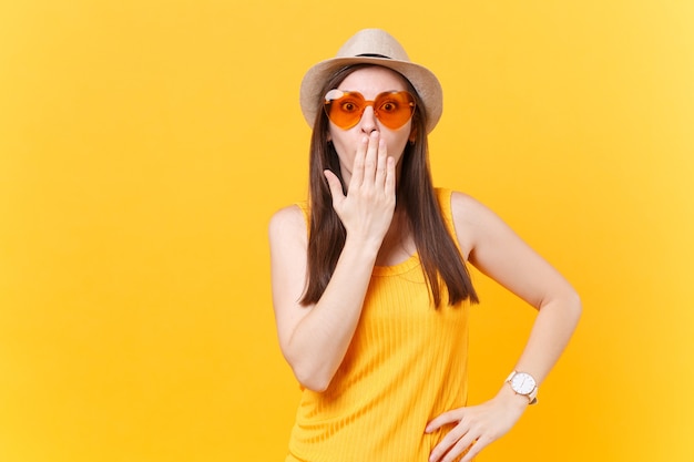 Portret zszokowana zabawa szalona młoda kobieta w słomkowym letnim kapeluszu, pomarańczowe okulary pokrywają usta dłoni, kopia przestrzeń na białym tle na żółtym tle. Ludzie szczere emocje, koncepcja stylu życia. Powierzchnia reklamowa.