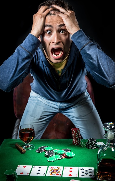 Zdjęcie portret zszokowanego mężczyzny stojącego przy stole do pokera z whisky na czarnym tle